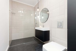 A minimalist bathroom with white tiles, a floating vanity, and a glass shower enclosure, maintaining a sophisticated and modern design.