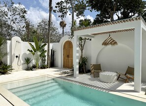 Outdoor area with a white swimming pool, white stone deck, a shaded outdoor lounge, and a shower