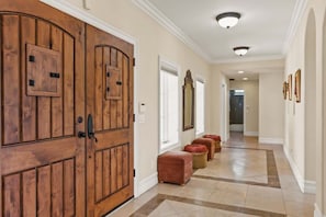 Step through the wooden door into a bright hallway with elegant light fixtures casting a warm glow. The hallway leads to a cozy nook with inviting window seats, perfect for relaxing and enjoying the serene views and natural light.
