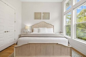 A serene bedroom with a plush bed, elegant decor, and large windows overlooking lush greenery.