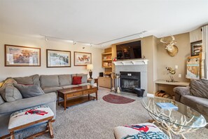 A warm and inviting living room with a rustic ski-lodge feel, featuring a cozy fireplace, a large sectional sofa, and ski-themed decor.