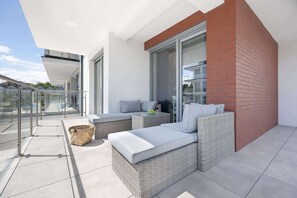 A spacious balcony with wicker furniture, cushions, and a brick accent wall.

