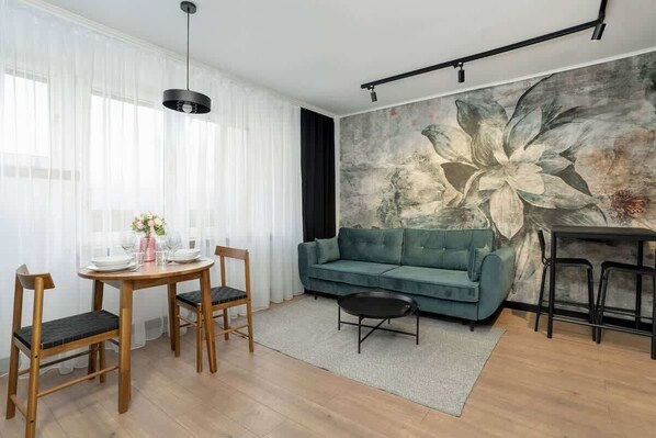 A stylish living and dining area with a large floral mural, a teal sofa, and a wooden dining table.

