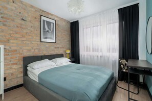 A cozy bedroom with an exposed brick wall, a teal bed, and black-out curtains.

