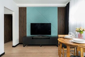 A sleek entertainment area with a teal accent wall, a TV, and a small wooden dining table.

