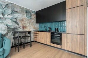 A modern kitchen with black and wooden cabinets, a teal backsplash, and a small dining table.

