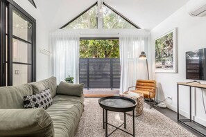  The studio's living space, bathed in natural light and opens out into the deck, is a cosy sanctuary with a sage green sofa and air-conditioning. 