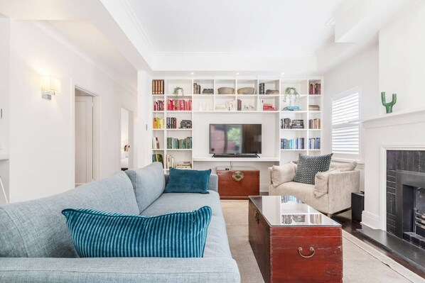 Unwind in the light-filled downstairs living space, a perfect blend of comfort and relaxation with a collection of books and a gas fireplace. 