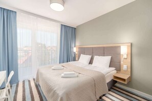 A cozy bedroom featuring a large bed with neutral bedding, wooden accents, and blue curtains, creating a calming atmosphere.
