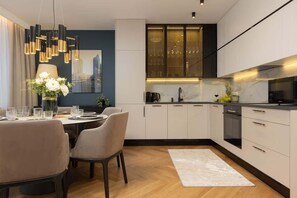 Open kitchen and dining area featuring sleek cabinets, a plush dining set, and a modern chandelier.
