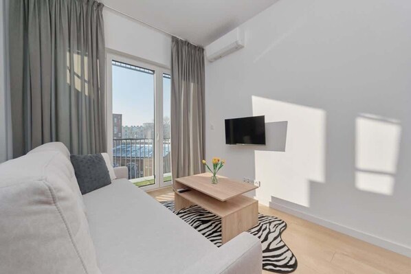 Living area with gray curtains, sofa bed, and light wooden flooring.