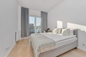 Spacious bedroom with large windows, gray bedding, and minimalist decor.