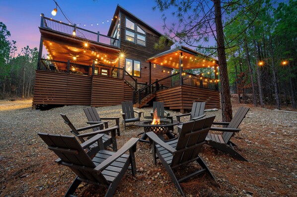 Outdoor firepit with adirondack chairs, string lighting and the back of the Counting Stars cabin in the background.