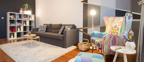 Living room with double sofa bed, armchair and shelf with books and decoration.