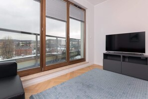 Living room with floor-to-ceiling windows, TV unit, and blue rug.

