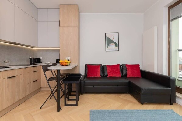 Living area with black sofa, wooden kitchenette, and a small dining table.
