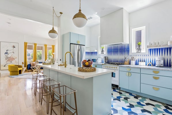 Bright, designer kitchen with bold blue backsplash, gold finishes, and a waterfall island—perfect for extended stays or filming.