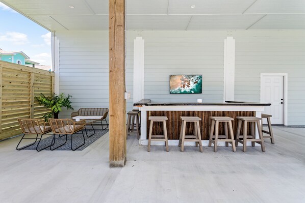 Outdoor tiki bar with TV & cozy seating area behind privacy wall.