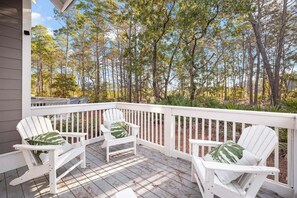 A peaceful balcony surrounded by lush trees, offering comfortable Adirondack chairs for enjoying the fresh air.