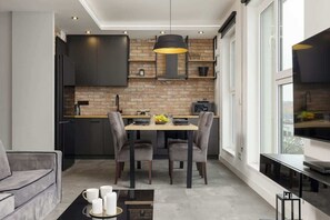 Open-concept kitchen and dining area with dark cabinetry, a wooden backsplash, and a modern chandelier.
