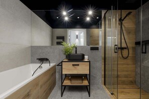 Luxurious bathroom with dark tiles, a glass-enclosed shower, and a floating wooden vanity.
