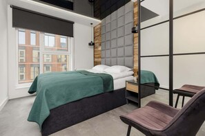 Cozy bedroom with a plush green bedspread, wooden paneling, and industrial-style lighting.
