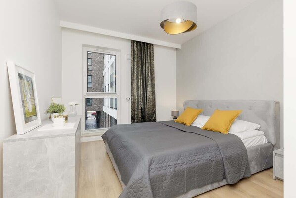 Stylish bedroom with a plush gray bed, golden accents, and a modern balcony view.