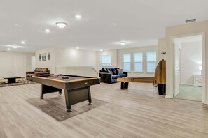 Enjoy endless fun in this spacious game room featuring a pool table, shuffleboard, and cozy seating area. Perfect for gatherings!