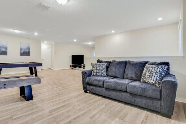 Relax and unwind in this spacious game room featuring a shuffleboard table and large TV, perfect for entertaining guests.