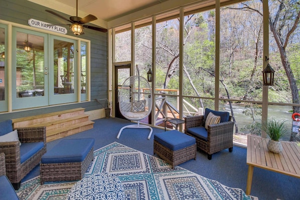 A cozy screened-in porch that overlooks the river, offering a perfect blend of comfort and nature. Enjoy the soothing sound of the water from the hanging swing chair or relax in the stylish wicker seating — an ideal spot to unwind with a morning cup