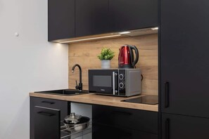 A close-up of the kitchen area showcasing a black microwave, a red kettle, and potted greenery, adding a warm and functional touch to the space.
