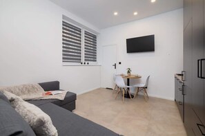 A contemporary living area featuring a comfortable gray sofa, a small wooden table, and a wall-mounted TV, offering a relaxing and functional space.
