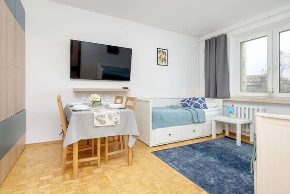 A cozy and modern living space with a stylish wooden dining table, a blue accent sofa, and a mounted TV, creating a functional yet inviting atmosphere.

