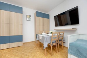A bright and spacious living area with a sleek wooden cabinet, a mounted TV, and a small dining space, combining aesthetics and practicality.

