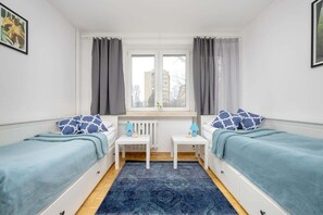A twin bedroom with fresh blue bedding, white furniture, and a plush blue rug, offering a comfortable and serene sleeping space.


