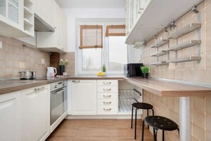 A compact yet charming kitchen with white cabinetry, open wooden shelves, and a dark wood countertop, giving it a rustic-modern appeal.

