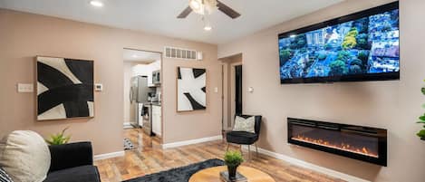 A welcoming living room with a flat screen TV, artwork, and electric fireplace