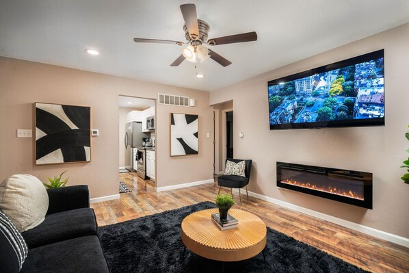 A welcoming living room with a flat screen TV, artwork, and electric fireplace