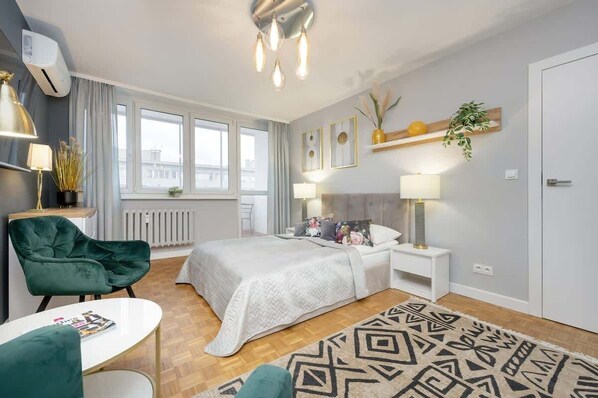 Stylish bedroom with a soft gray bedspread, a modern chandelier, and elegant green armchairs.
