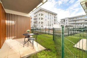 A cozy balcony with a small table and chairs, overlooking a green courtyard.

