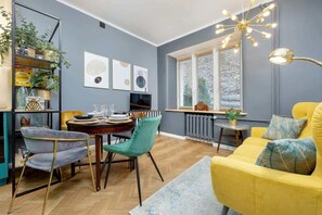A dining area with a round table, velvet chairs, and large windows letting in natural light.

