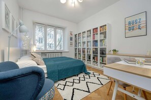 A cozy reading nook with a large window, bookshelves, and a soft blue daybed.

