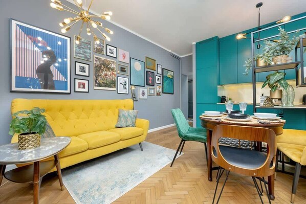 A stylish living room with a yellow sofa, gallery wall, and turquoise kitchen cabinets.

