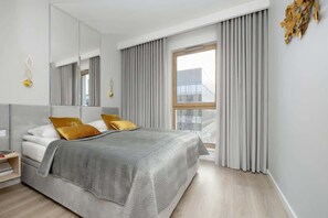 A stylish bedroom with a cozy queen-size bed adorned with soft yellow and gray bedding. The room is filled with natural light thanks to large windows and features a peaceful, neutral color palette with a touch of modern design.