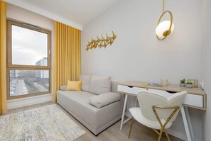 This bedroom features a compact but comfortable space with a double bed. A bright yellow throw adds a pop of color, while a sleek, modern wall light and art piece enhance the room’s cozy feel.