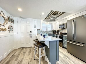 This contemporary kitchen features sleek appliances, a large island with seating, and charming coastal décor, making it perfect for preparing meals in a relaxing beachside atmosphere.