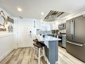 This contemporary kitchen features sleek appliances, a large island with seating, and charming coastal décor, making it perfect for preparing meals in a relaxing beachside atmosphere.