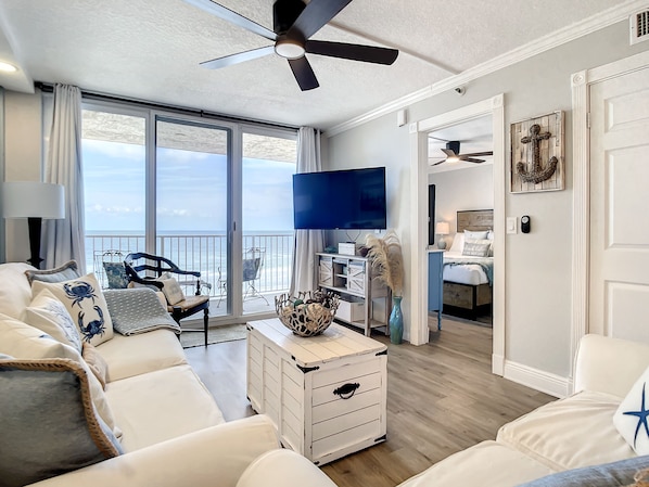 Bright living area with oceanfront balcony access, cozy seating, and a large flat-screen TV.