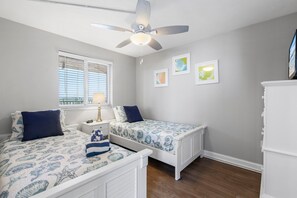 Cozy twin bedroom with shell-patterned bedding, vibrant artwork, and natural light.