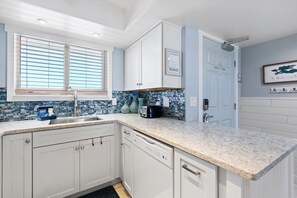 Prepare meals with ease in a bright kitchen featuring quartz counters, ocean-inspired backsplash, and modern appliances.